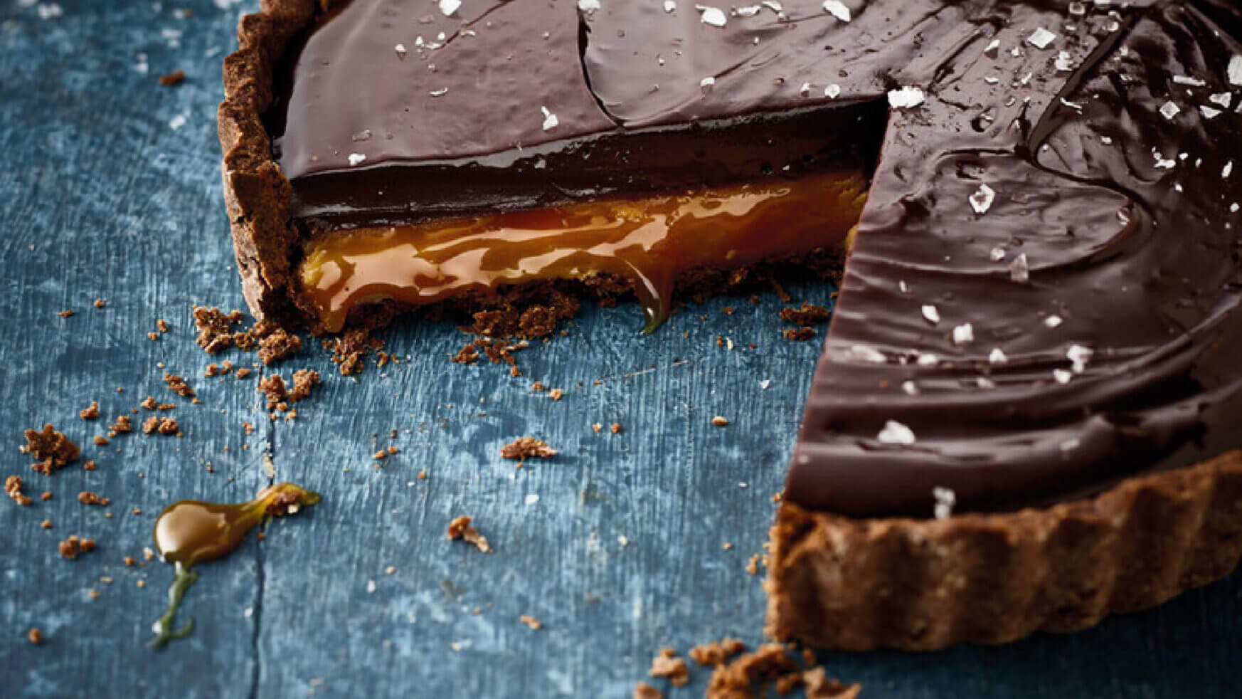 Een in punten gesneden chocolade-karameltaartje, waarvan het smeuïge midden zichtbaar is, bedekt met zeezoutvlokken op een blauw oppervlak.