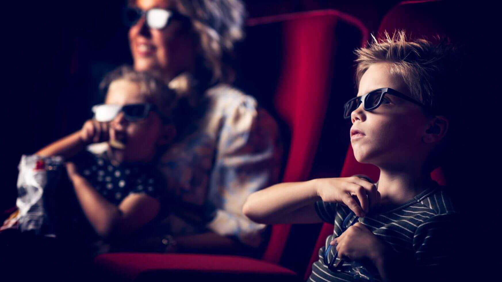 Een gezin met een 3D-bril kijkt aandachtig in een donkere bioscoopzaal. Een kind houdt popcorn vast.
