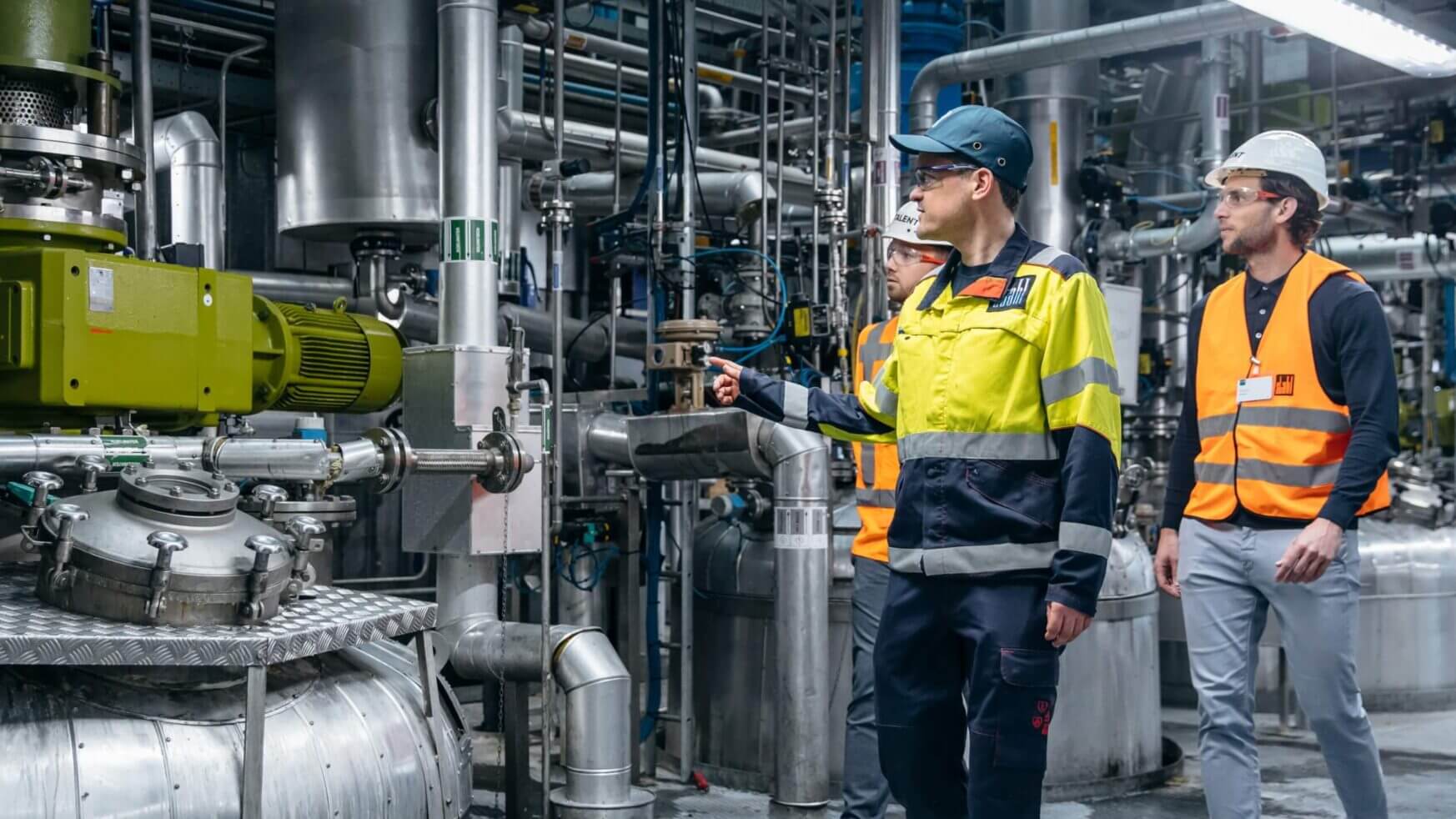 Drie werknemers in veiligheidskleding inspecteren de machines in een fabriek.