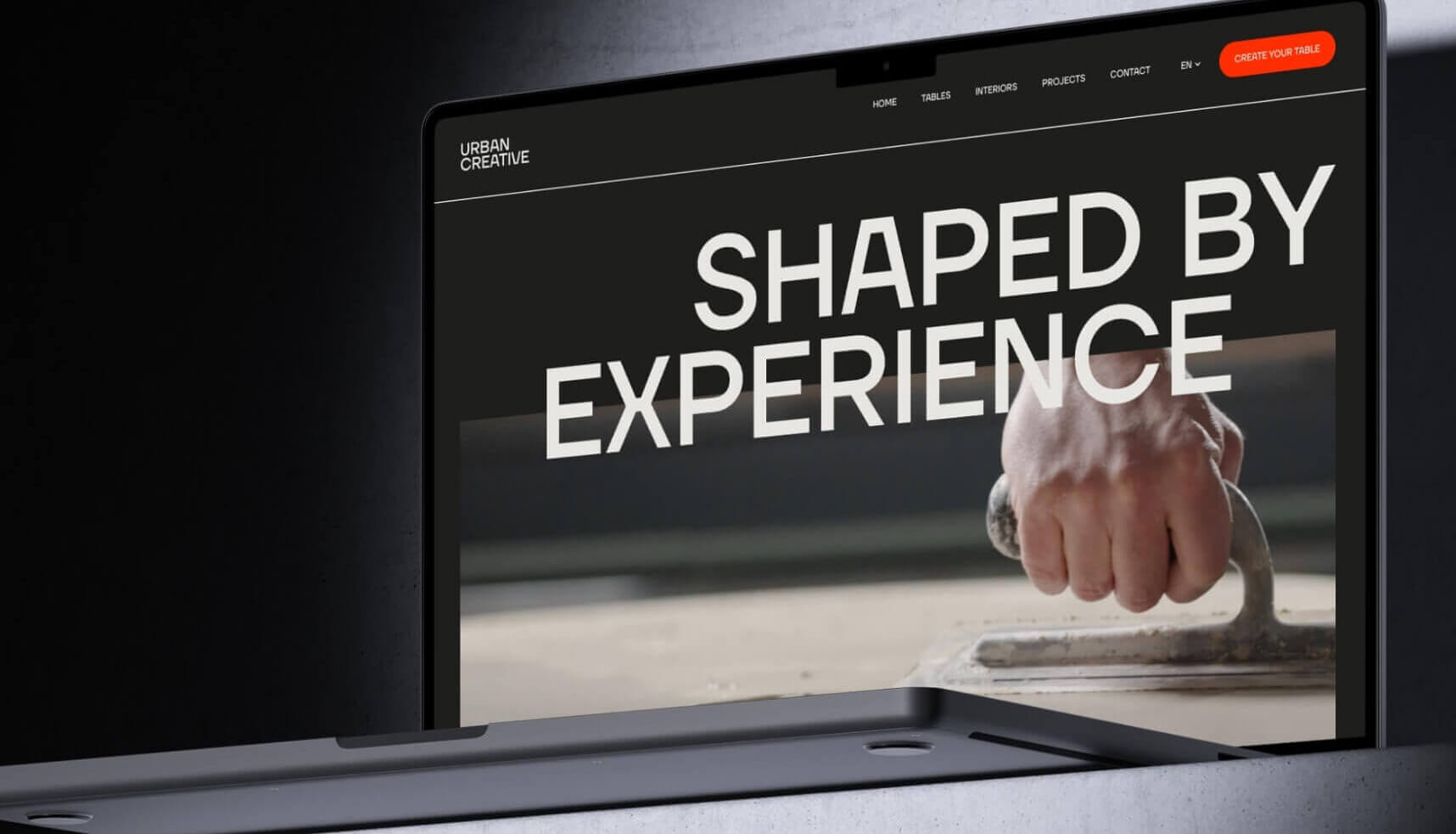 Op een laptop verschijnt een website met de tekst 'Shaped by Experience' en een afbeelding van een hand die een troffel gebruikt.