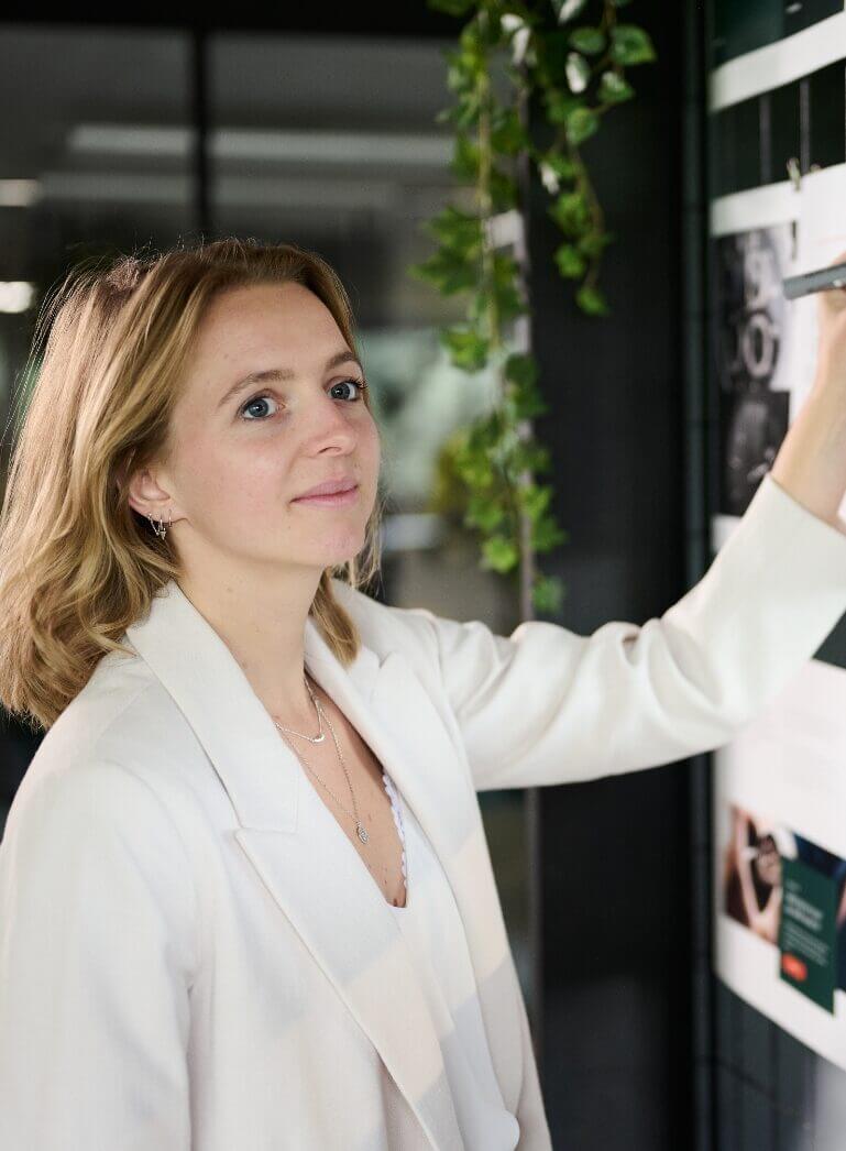 Een persoon in een wit jasje bekijkt binnenshuis een displaybord bij een hangplant.