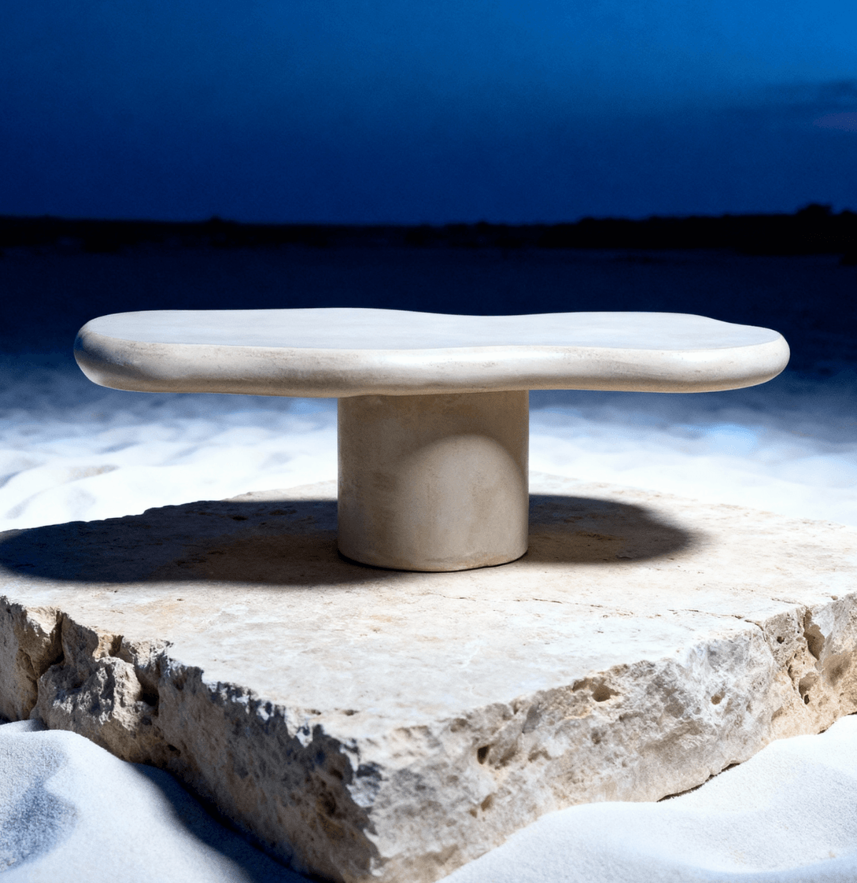 Moderne stenen tafel op een vierkante plaat rust op wit zand onder een schemerige hemel.