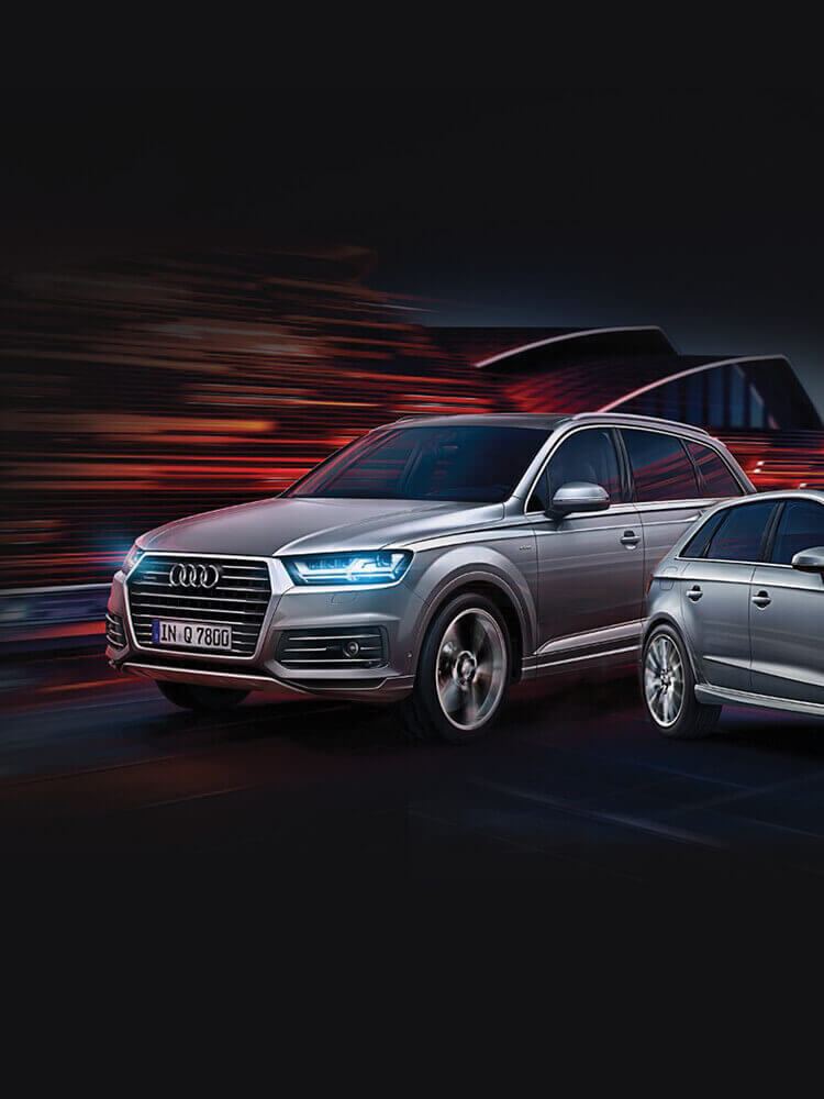 Een zilveren SUV en een gestroomlijnde sedan racen door de nacht en belichamen de stijl en prestatiegerichtheid van Audi Roosendaal.