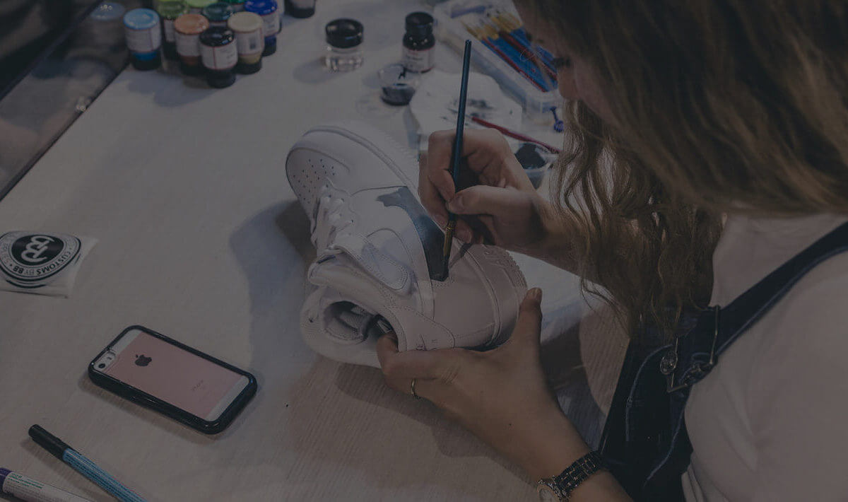 De kunstenaar schildert een sneaker in felle kleuren, met zijn smartphone in de buurt; zo ontstaat Customs by BB.