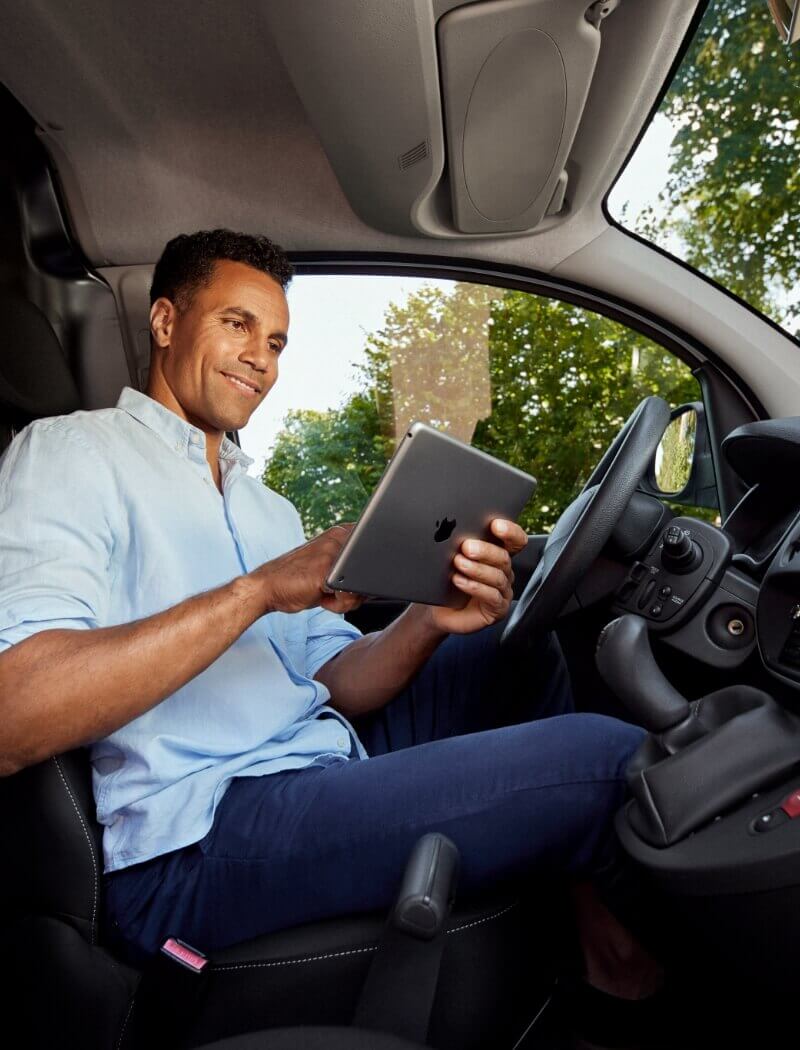 Chauffeur in een lichtblauw shirt gebruikt een tablet terwijl hij in de auto zit.