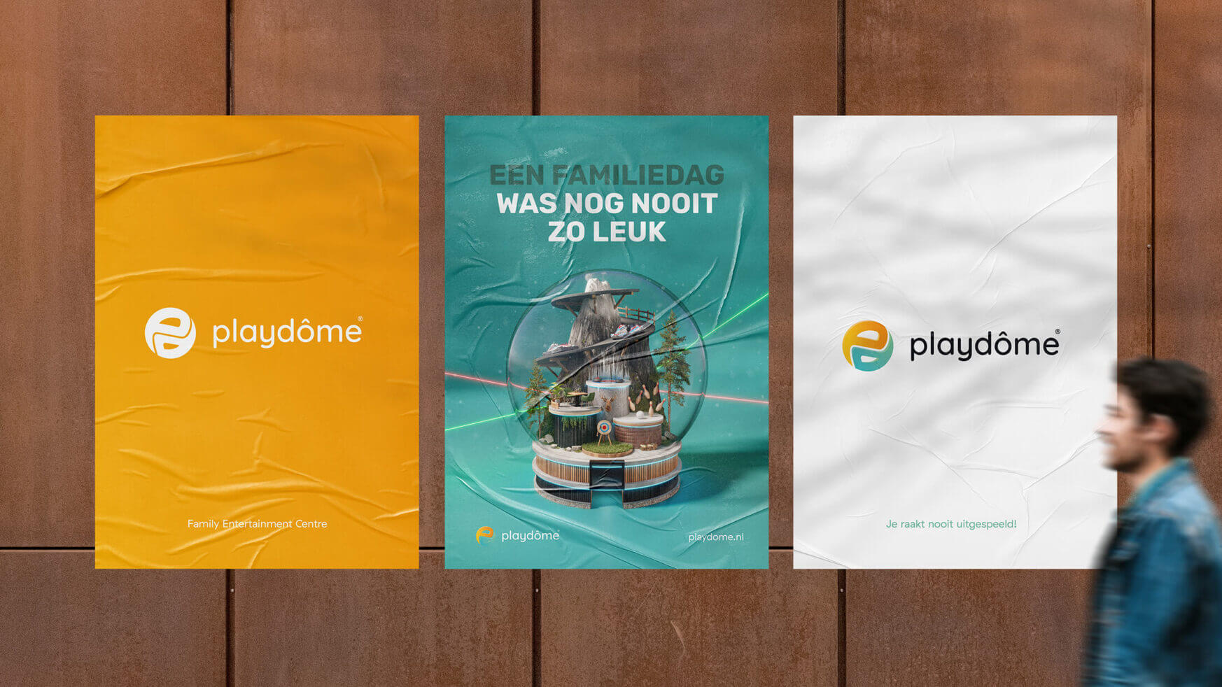 Een man loopt langs drie posters op een muur, waarvan er twee het logo van Playdôme dragen.