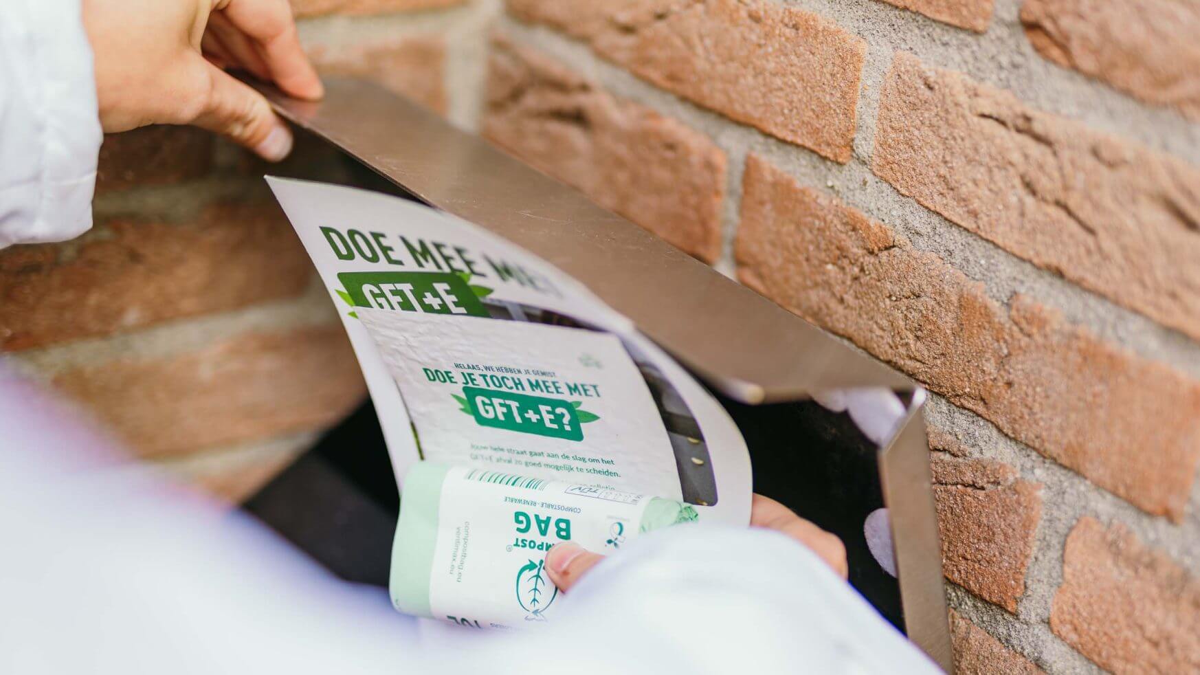 Met de hand groene en witte flyers en een "RSD aan de bak!" folder in een metalen brievenbus in een bakstenen muur stoppen.