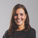 Lachend persoon, bruin haar, zwart topje, ketting, grijze achtergrond.