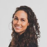 Lachende vrouw met krullend bruin haar in een zwart topje tegen een witte achtergrond.