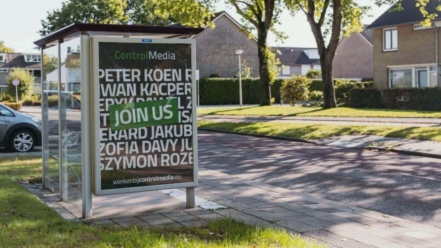Poster bij bushalte: "Word lid van Control Media!" Woonstraat en huizen op de achtergrond.
