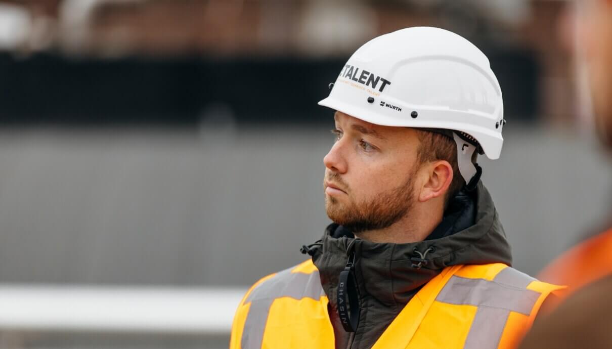 Bouwvakker in een geel vest en helm, kijkt opzij.