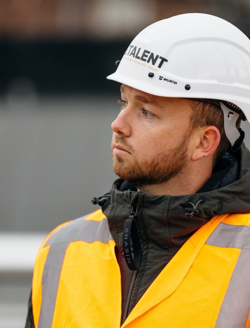 Bouwvakker met witte helm en oranje vest, kijkt opzij.