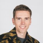 Grijnzend in camouflagekleding tegen een minimalistische achtergrond.