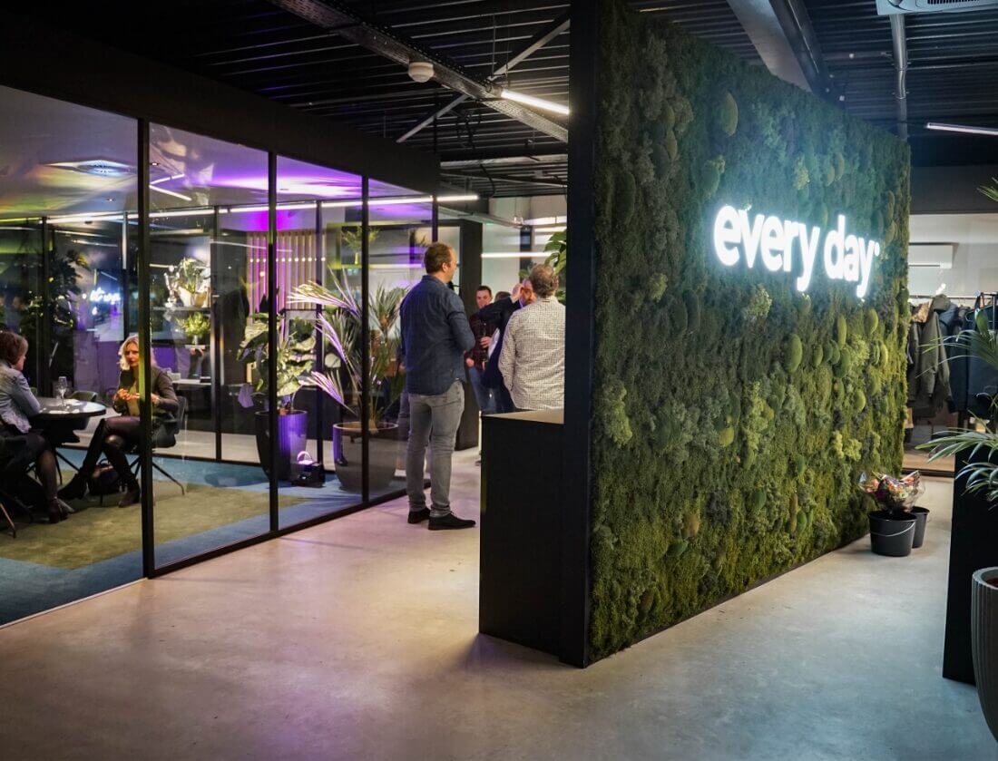 Bruisend kantoor met een neonverlichte plantenwand en een glazen vergaderruimte.