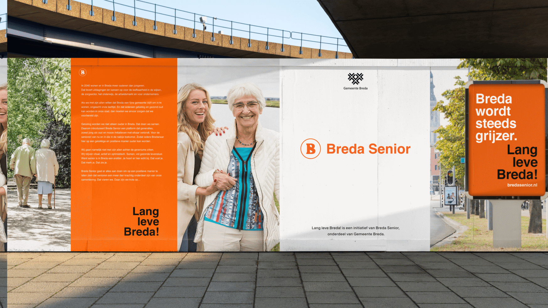 Een oudere volwassene en een jongere vrouw lachen naast een poster van Breda Senior onder een brug in Roosendaal.