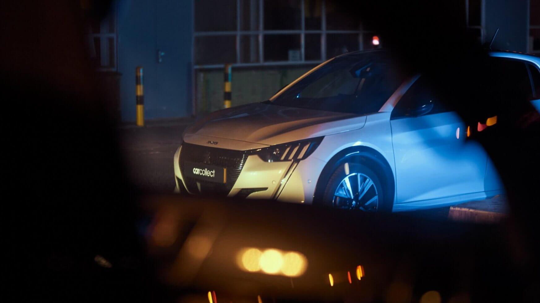 Een witte Peugeot e-208 onder nachtverlichting legt de essentie van stedelijke elegantie vast voor autoliefhebbers.