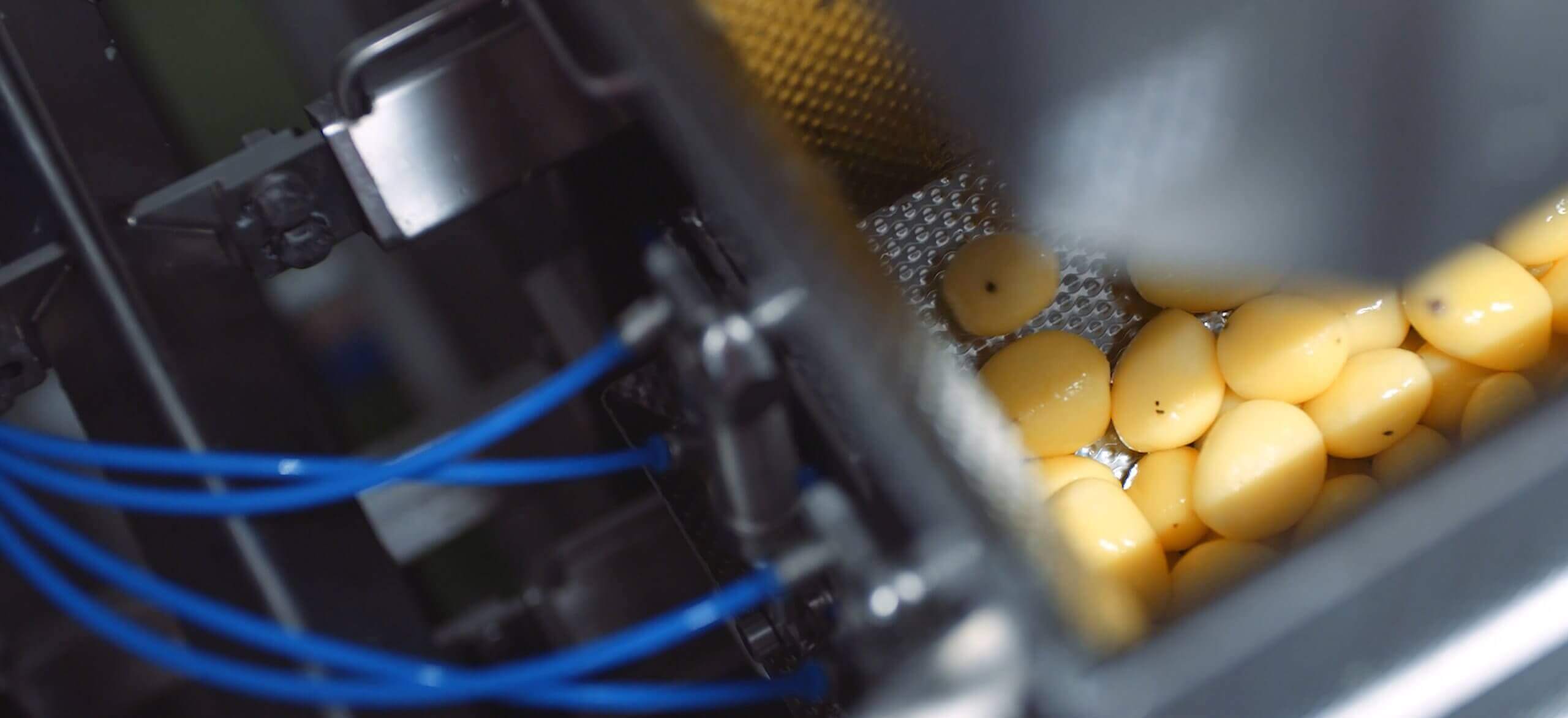 Close-up van een machine die gele tabletten sorteert, blauwe kabels zichtbaar aan de zijkant.