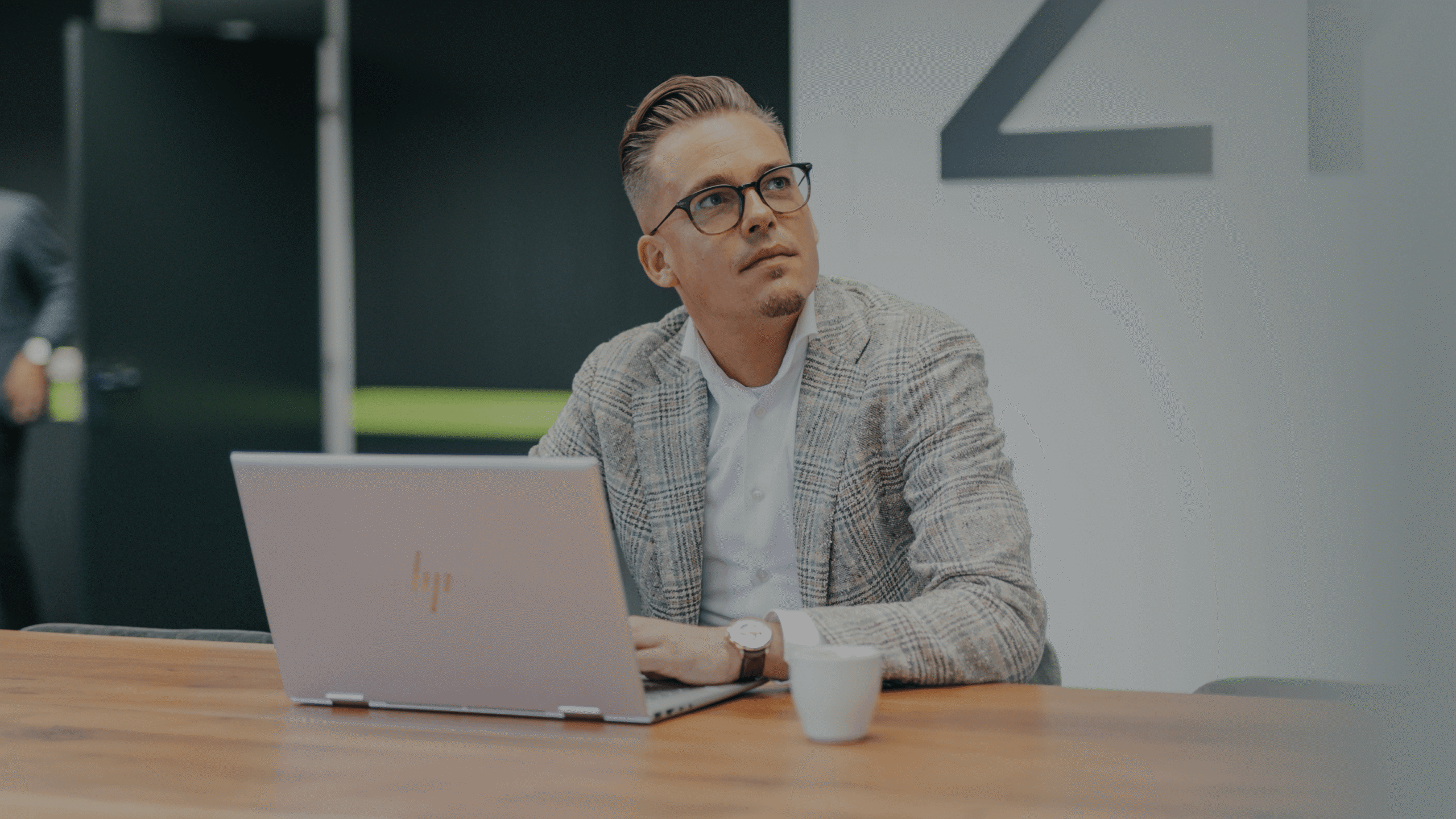 Een man met bril gebruikt een laptop aan een strak houten bureau in een modern kantoor.