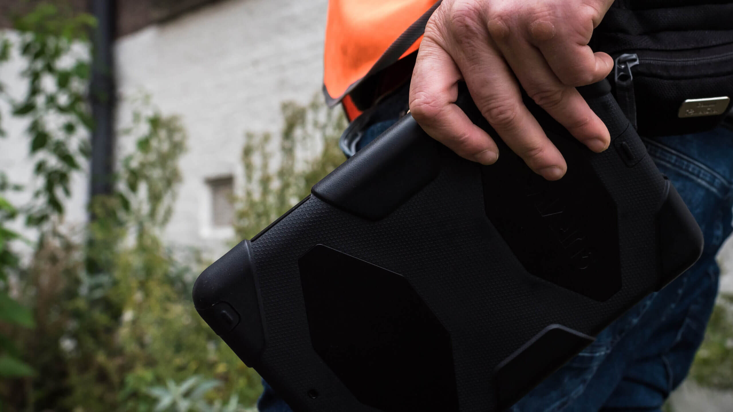 Een TB-expert in een oranje vest houdt buiten een robuuste tablet vast.