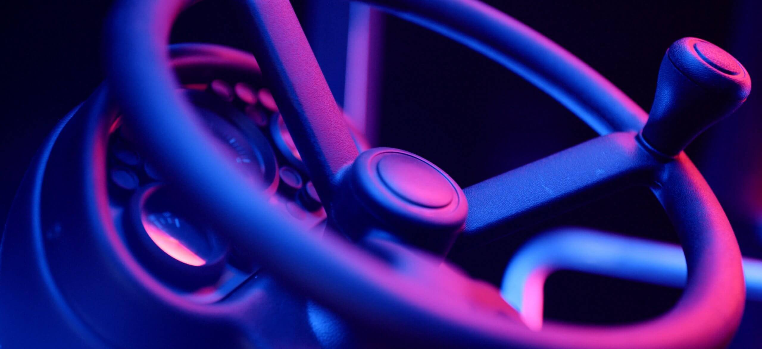 Het stuurwiel gloeit in fel paars en blauw neonlicht.