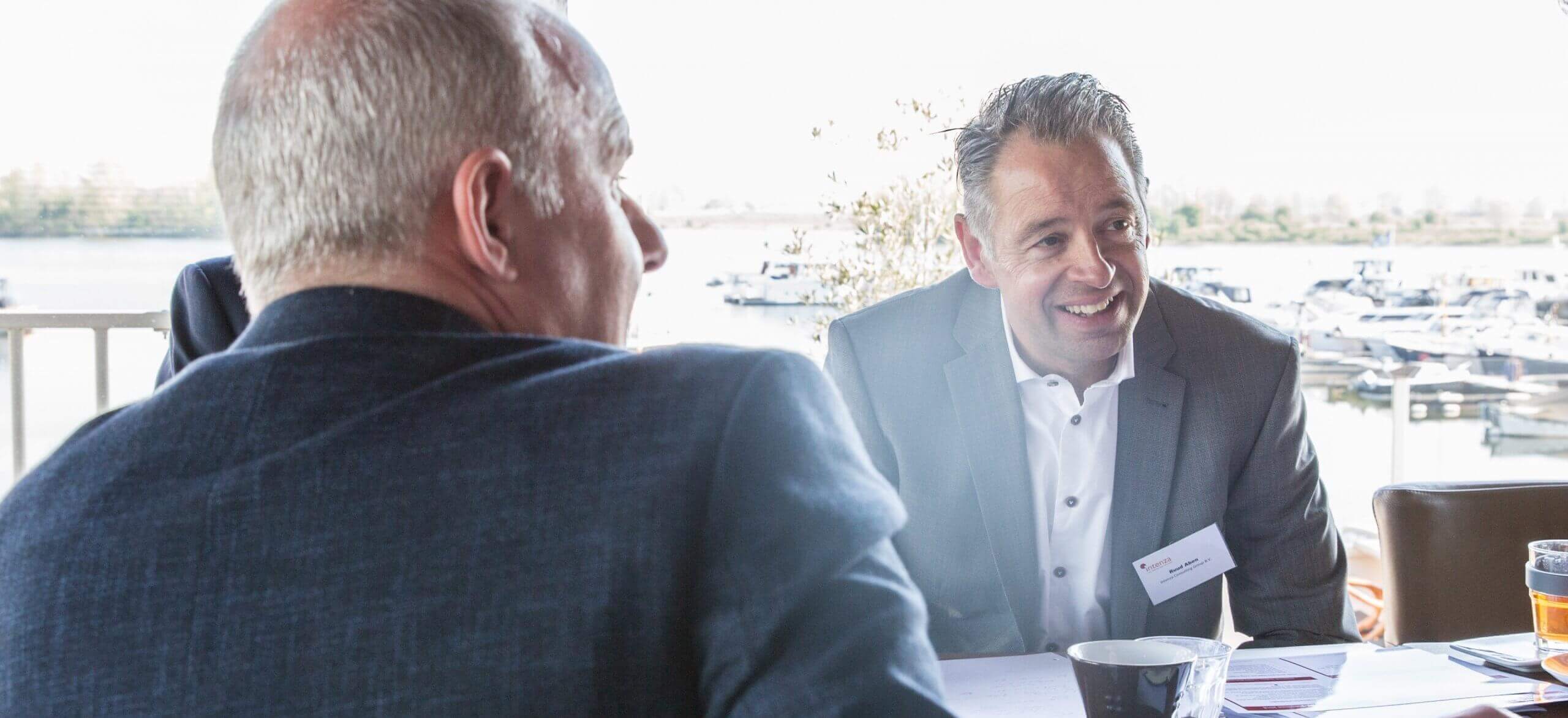 Twee zakenmannen praten bij een raam met uitzicht op de jachthaven.