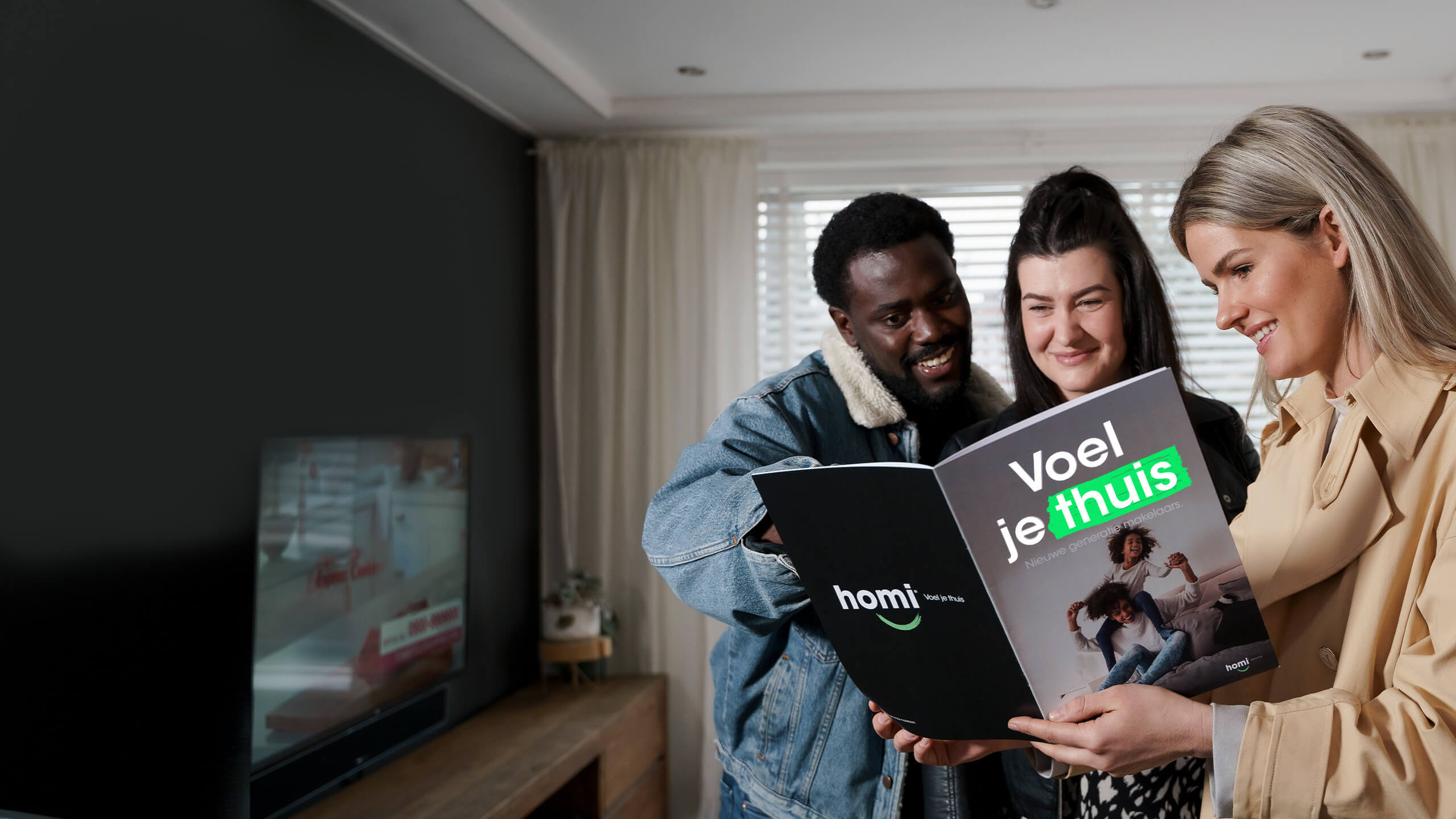 Drie mensen in een huiskamer lachen terwijl ze het tijdschrift 'Voel je thuis' lezen.