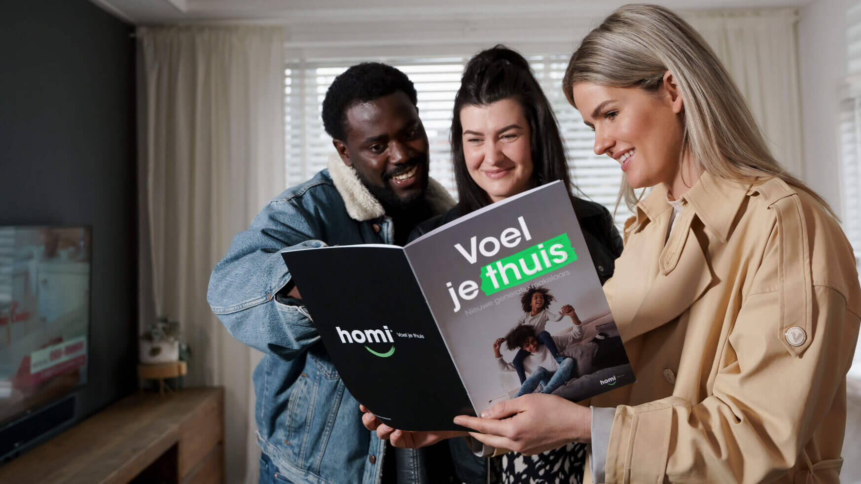 Drie mensen glimlachen bij een 'Voel je thuis'-brochure in een lichte woonkamer.