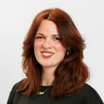 Persoon met lang, golvend bruin haar in een zwart topje glimlacht tegen een witte achtergrond.