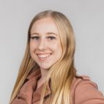 Blond, lachend, bruin jasje; effen achtergrond.