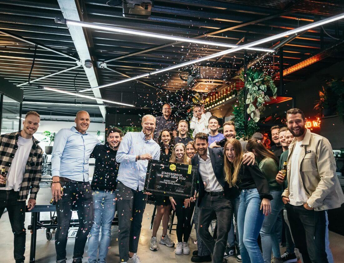 Een vrolijke groep binnen, lachend naar de camera, terwijl er confetti naar beneden vliegt.