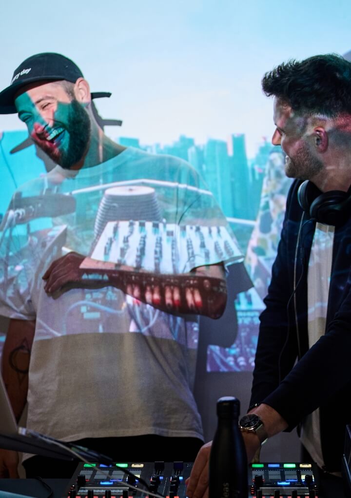 DJ's grijnzen terwijl ze muziek draaien op een achtergrond van stadsbeelden.
