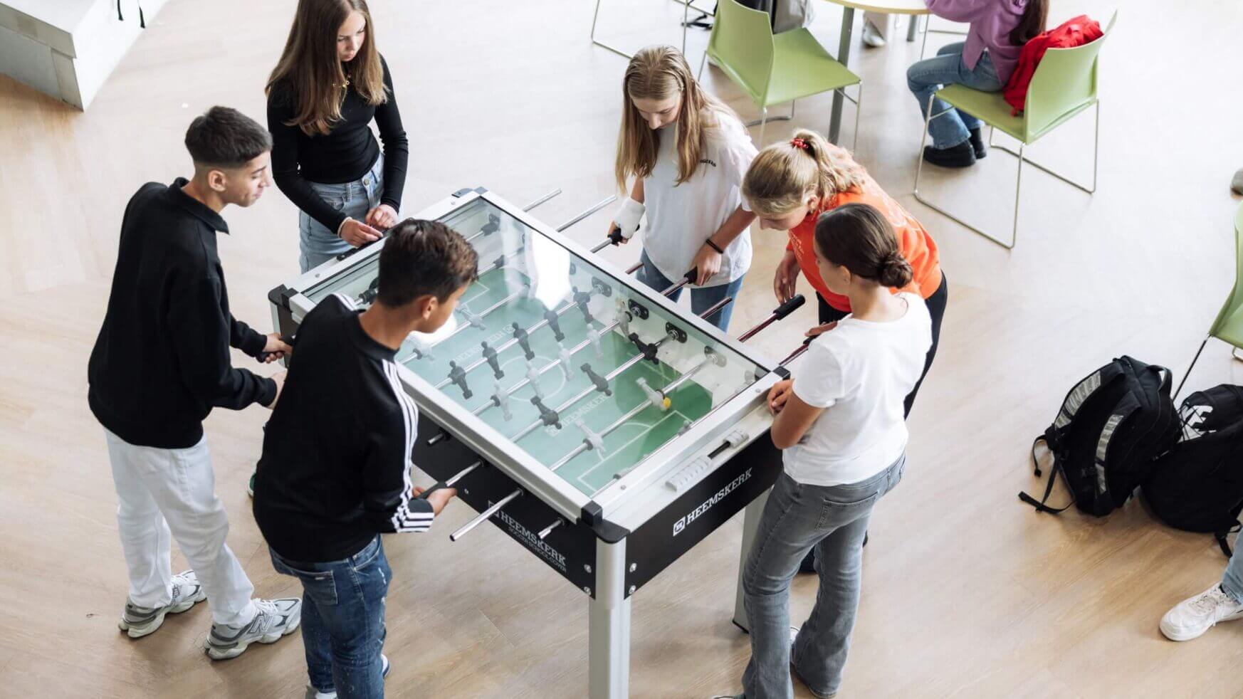 Jongeren spelen tafelvoetbal in een lichte kamer, anderen ontspannen zich aan een tafeltje ernaast.