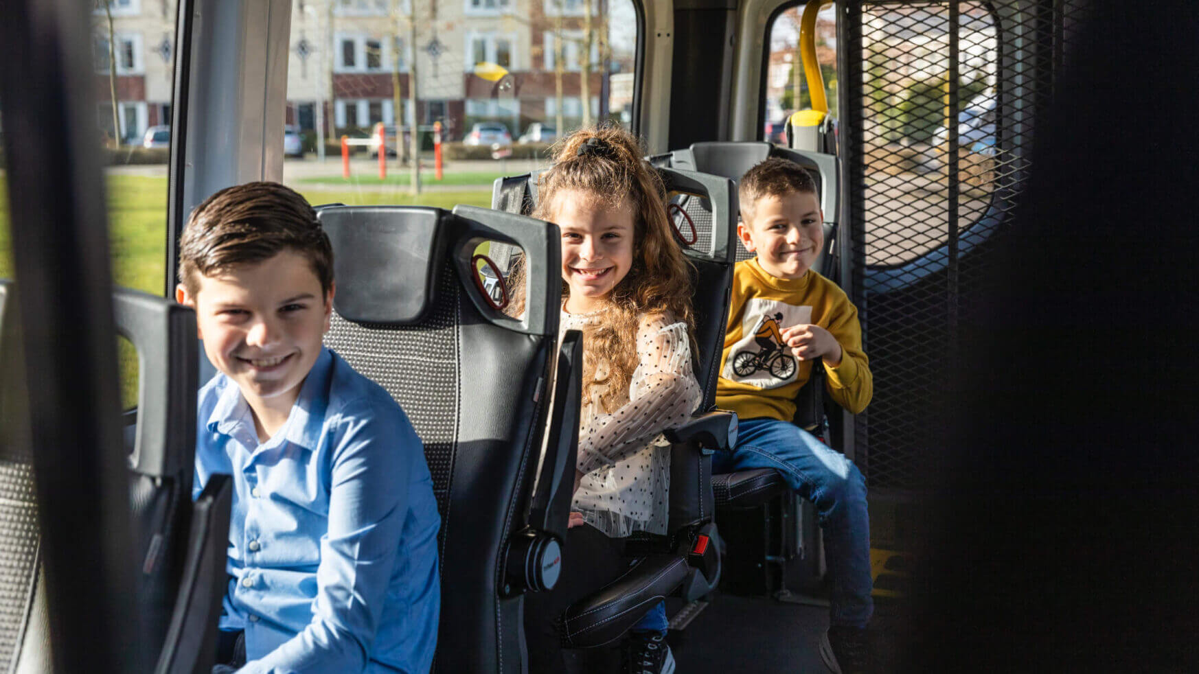 Drie lachende kinderen in een taxi: een jongen vooraan, een meisje in het midden en nog een jongen met een speelgoedcamera.