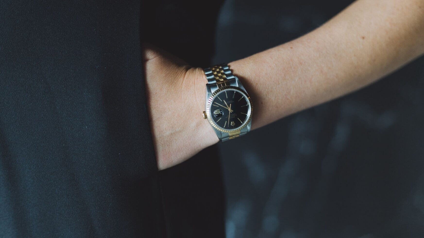 Hand in zak, zwart en zilver horloge tegen een donkere achtergrond.