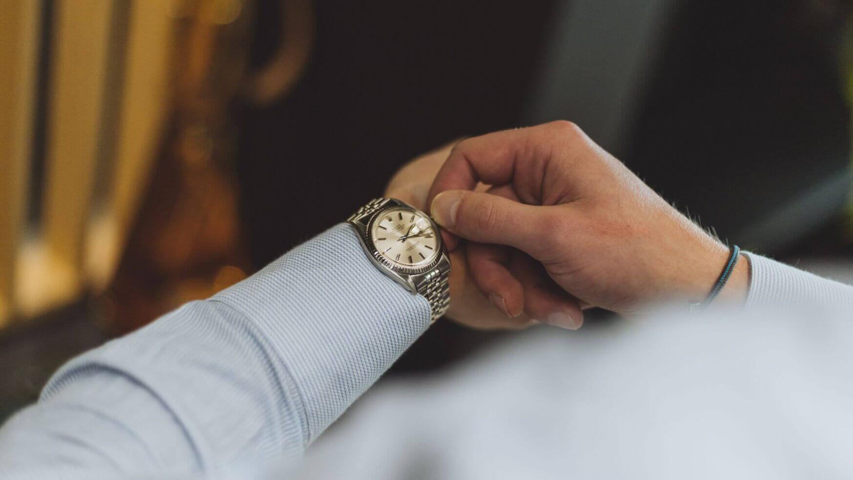 Iemand kijkt op zijn zilveren metalen horloge om te zien hoe laat het is.