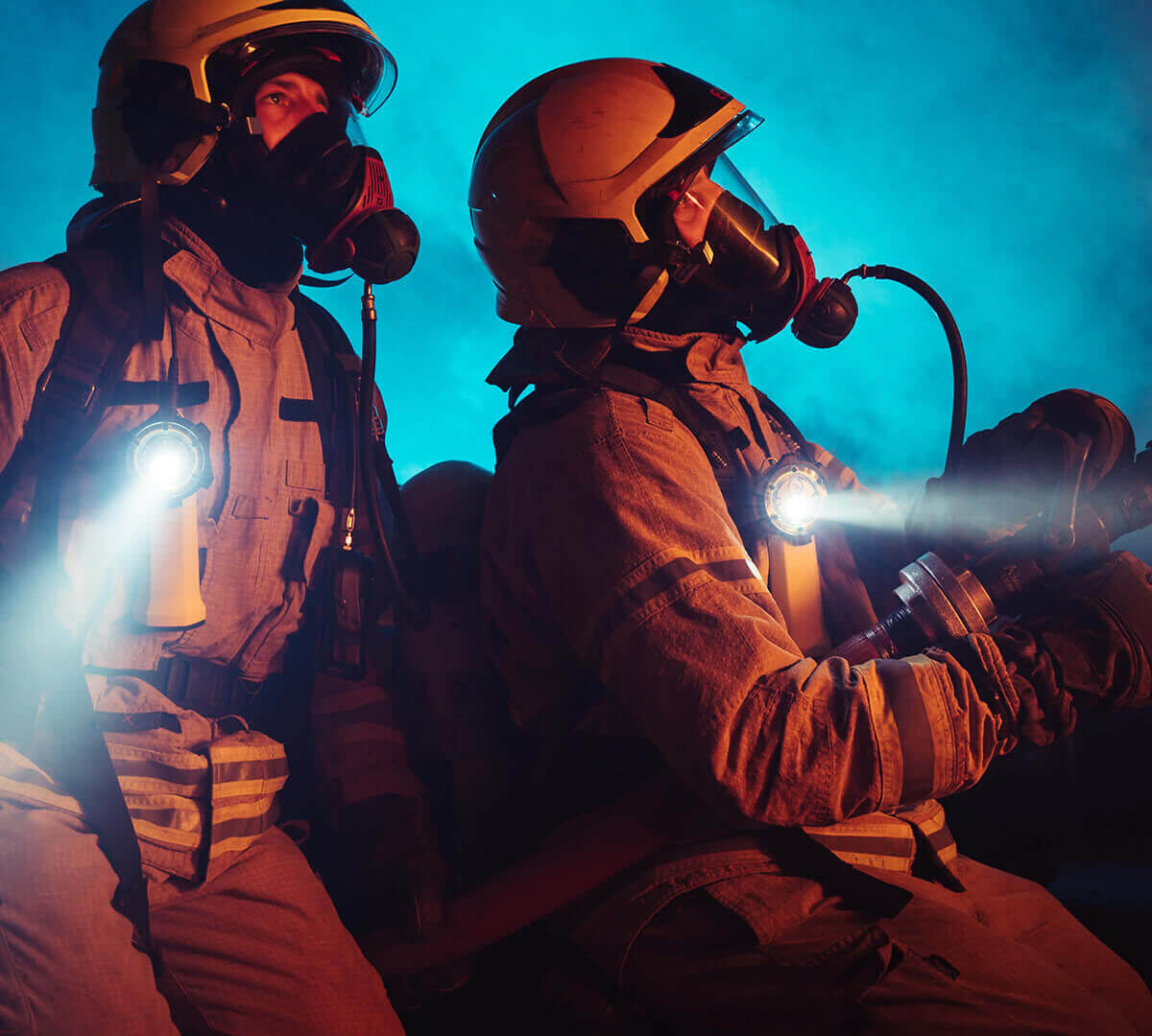 Twee brandweermannen, uitgerust met zaklampen, doorboren de rokerige duisternis met een griezelig schijnsel in hun kielzog.