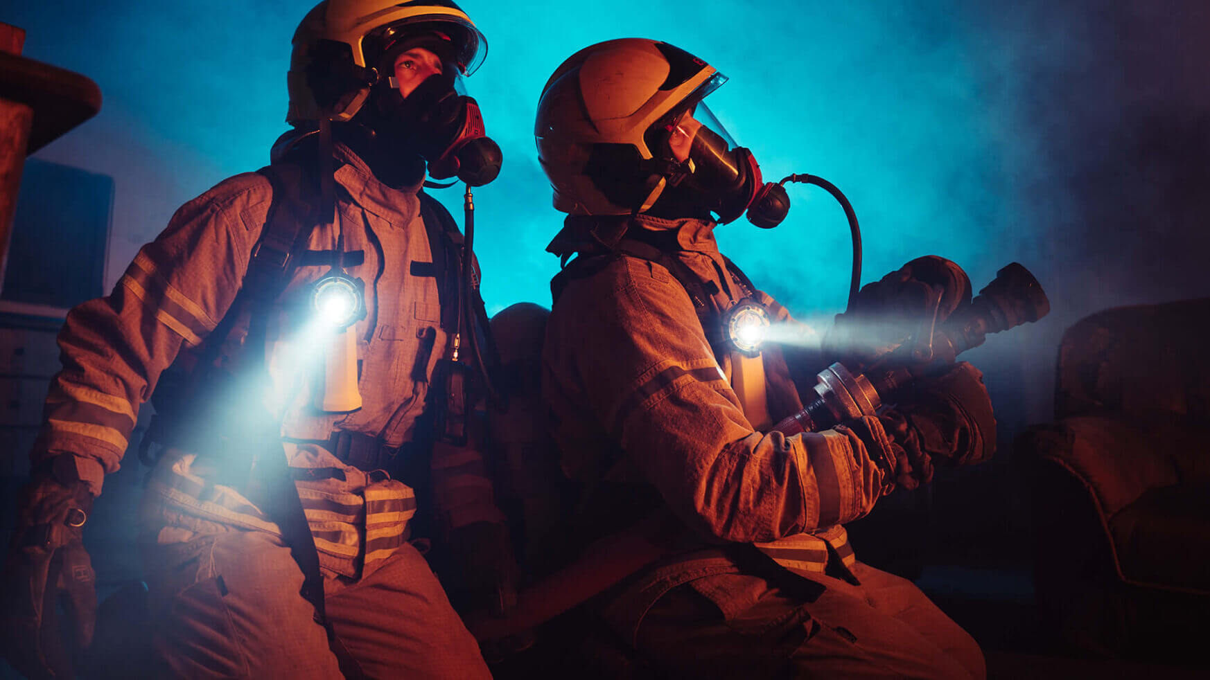 Twee brandweermannen, uitgerust met zaklampen, doorboren de rokerige duisternis met een griezelig schijnsel in hun kielzog.