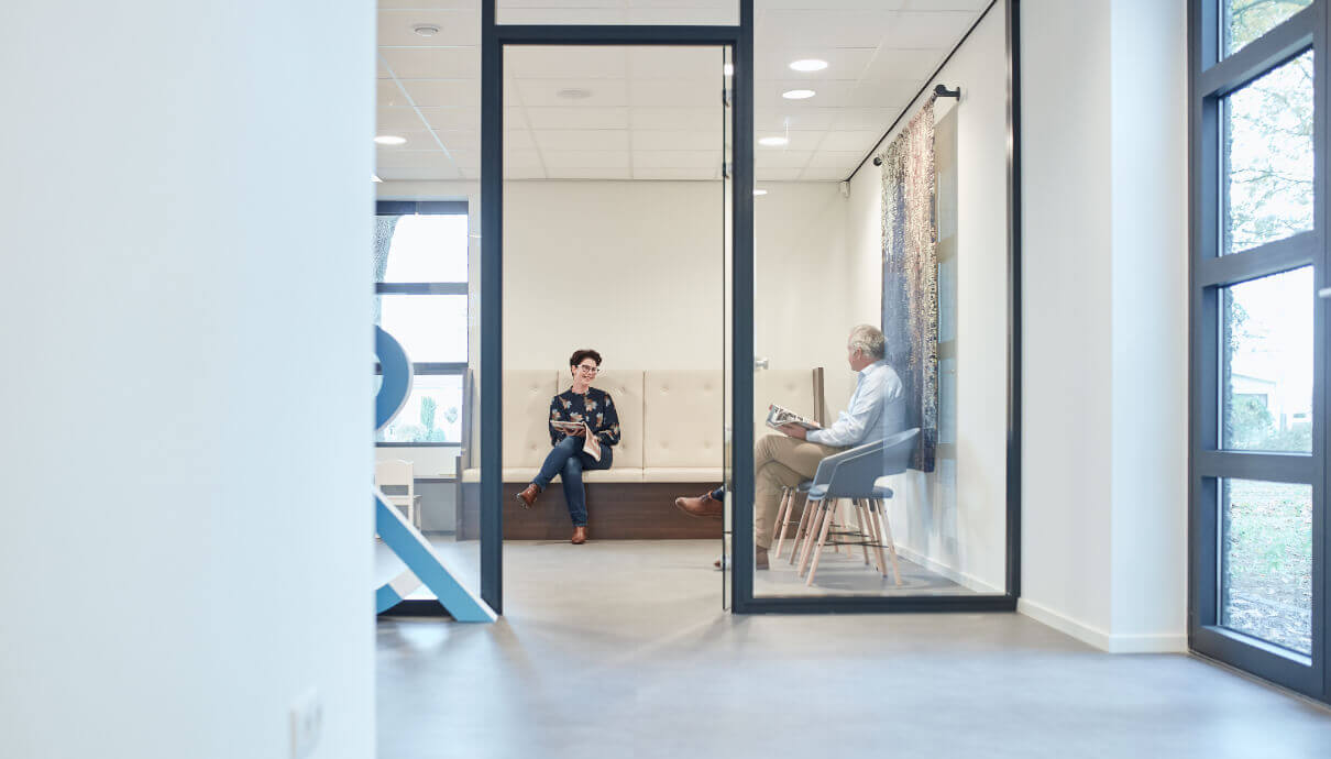 Twee mensen praten in een strak kantoor met glazen wanden en een minimalistische inrichting.