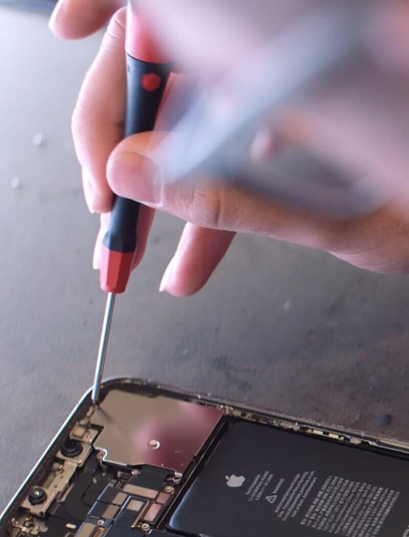 Iemand repareert vakkundig een smartphone met een schroevendraaier, wat blijk geeft van zijn/haar Touchfix-vaardigheden.