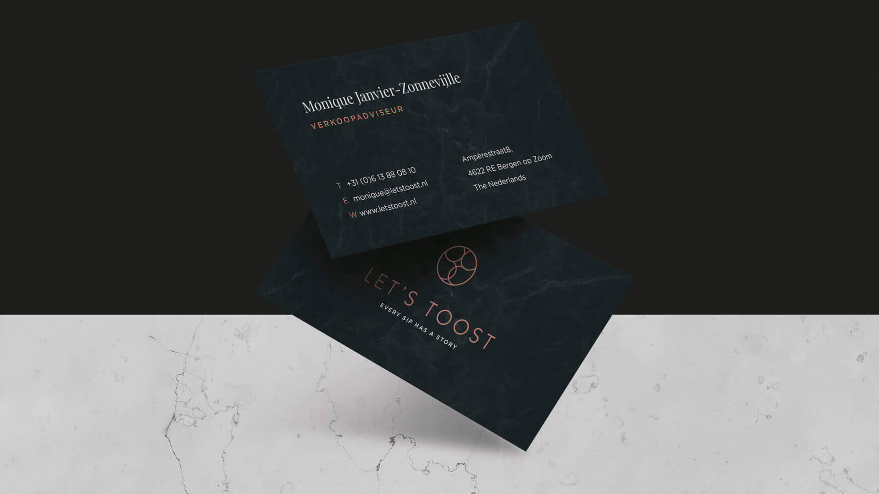 Twee strakke, donkere Lets Toost-visitekaartjes op marmer.