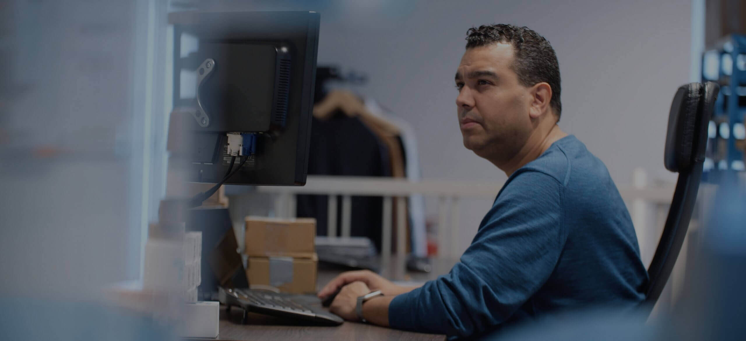 Iemand in een blauw shirt zit geconcentreerd te werken aan een bureau, omringd door kartonnen dozen en een Touchfix-computer.