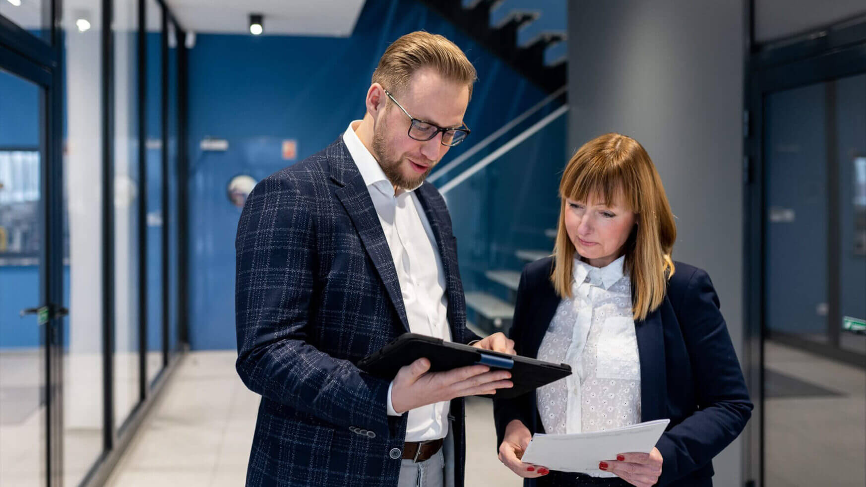 Een man en een vrouw bespreken documenten in de strakke hal van het kantoor van Viscon Group.