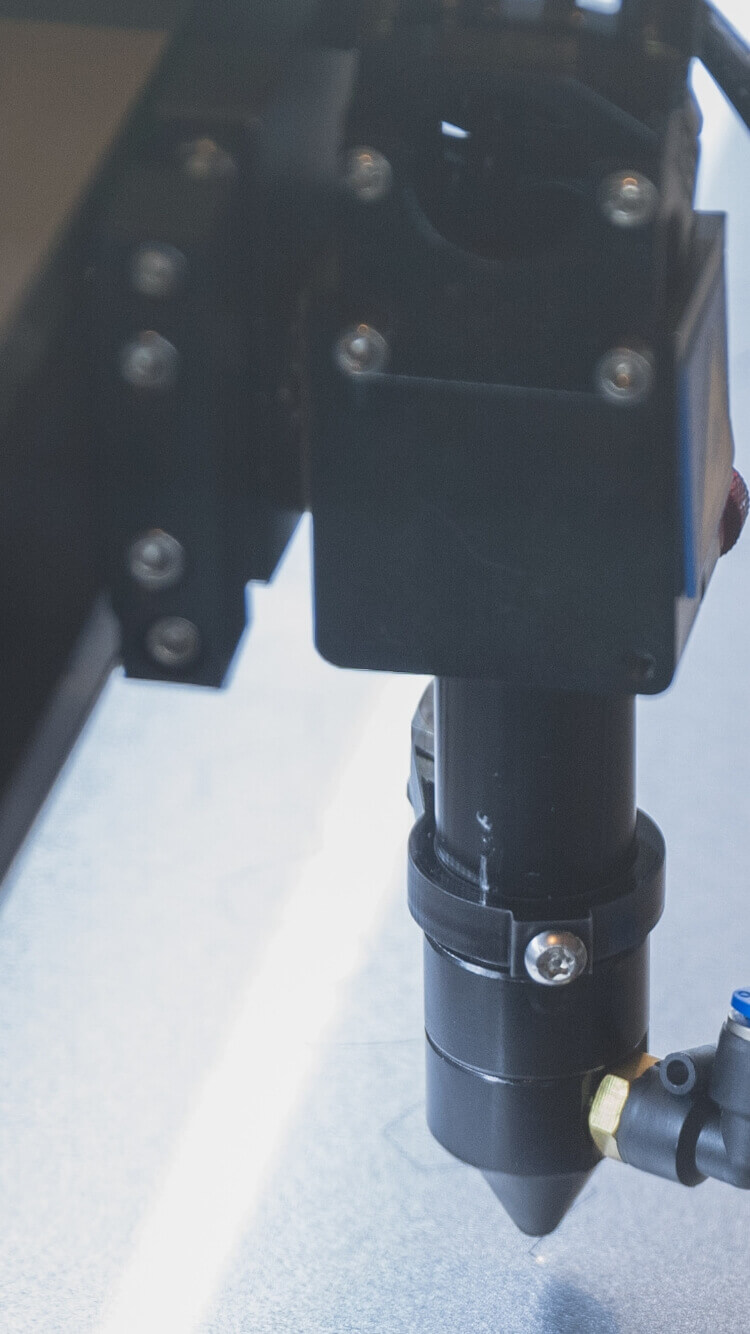 Close-up van een Vrotech-machineonderdeel: schroeven en spuitmond, waarschijnlijk van een CNC- of lasersnijder.