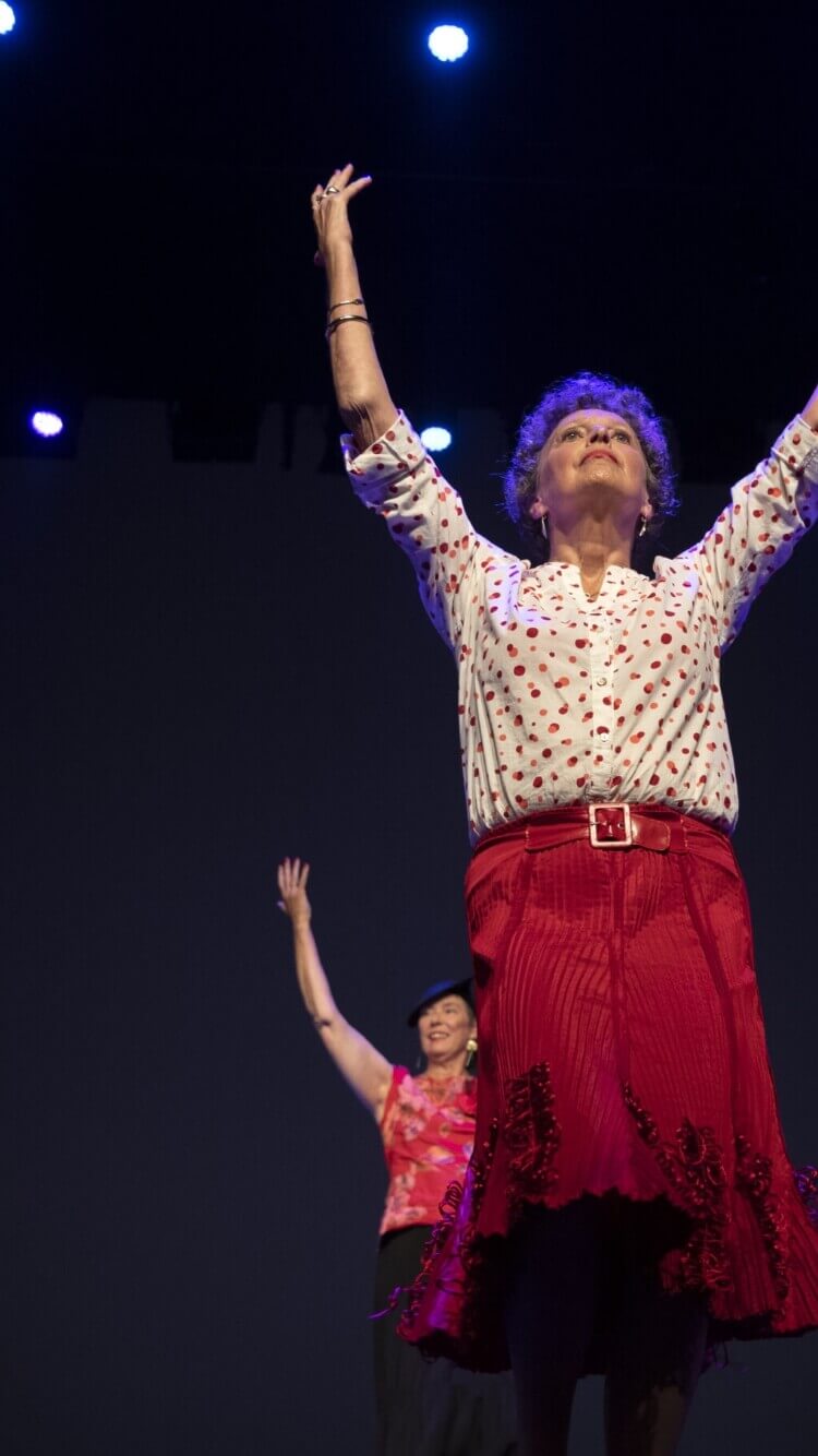 Twee vrouwen dansen op het podium in gebloemde outfits onder blauwe lampen, met hun armen omhoog.