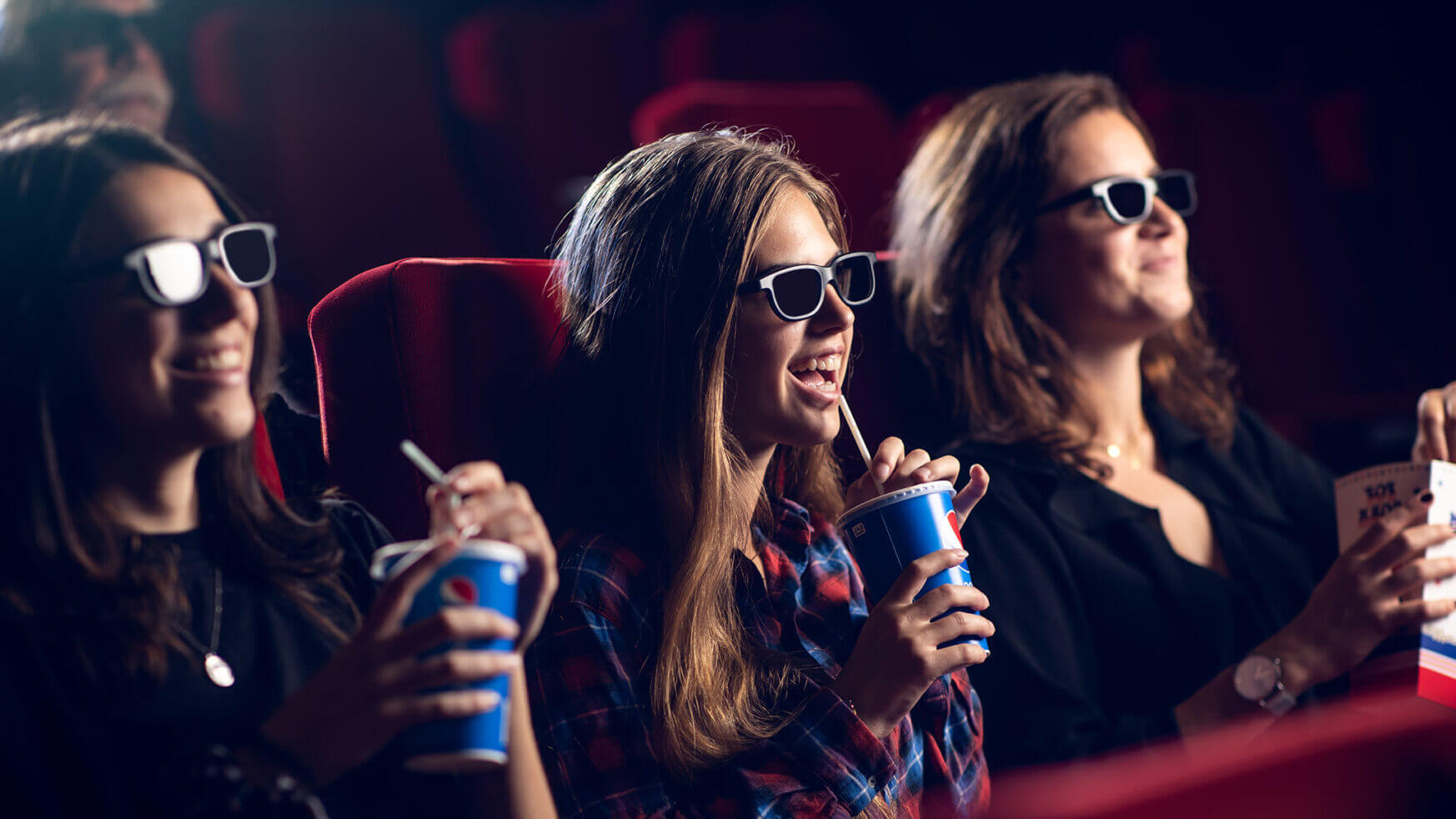 Drie vrienden met 3D-brillen genieten van popcorn en een drankje in de bioscoop.