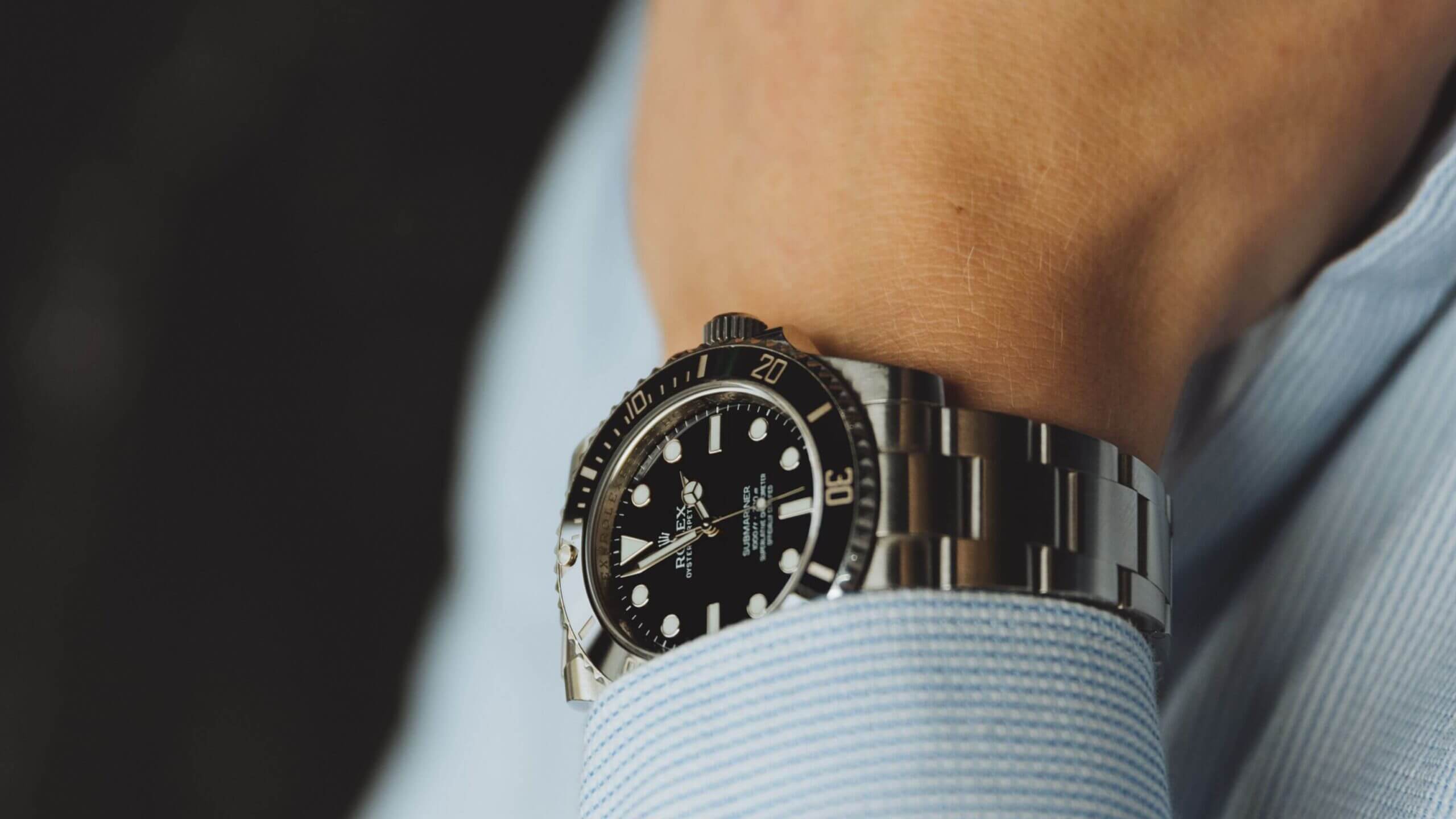 Close-up: Horloge van roestvrij staal, zwarte wijzerplaat, draaibare lunette, om de pols met een blauw shirt.