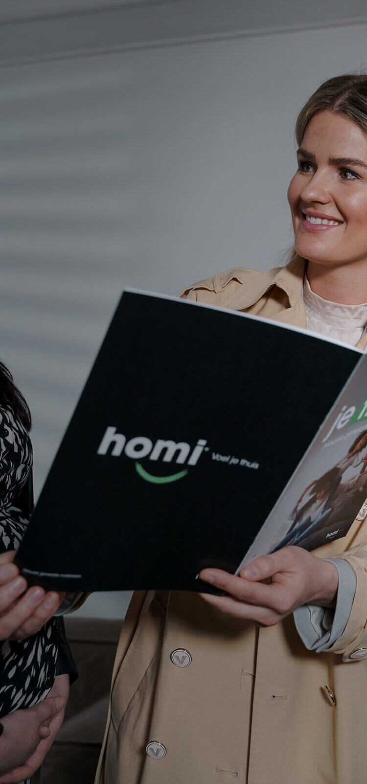 Lachende vrouw houdt een 'homi'-brochure vast en praat met iemand.