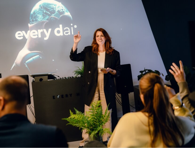 Een vrouw geeft een presentatie aan een publiek, staand bij een scherm waarop 'elke dag' wordt getoond.
