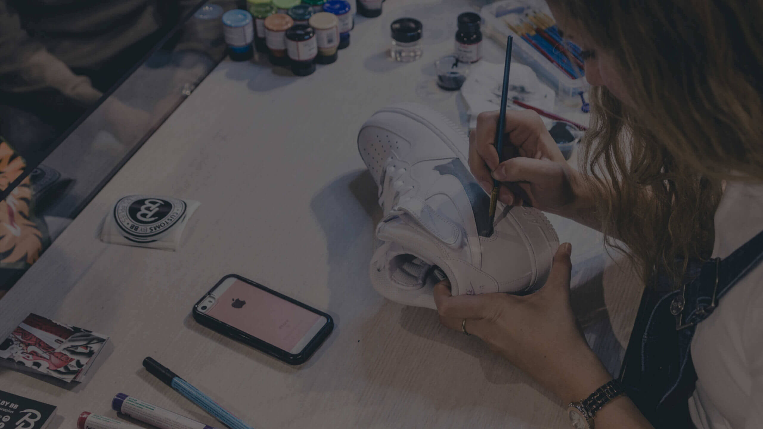 Tussen potten verf transformeert iemand een witte sneaker tot kunstwerk, geïnspireerd door Customs van BB op een nabijgelegen telefoon.