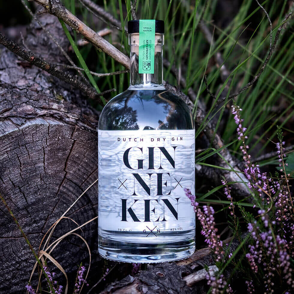 Een fles Nederlandse droge gin ligt stijlvol op boomstammen, tegen een achtergrond van groen gras en paarse bloemen.